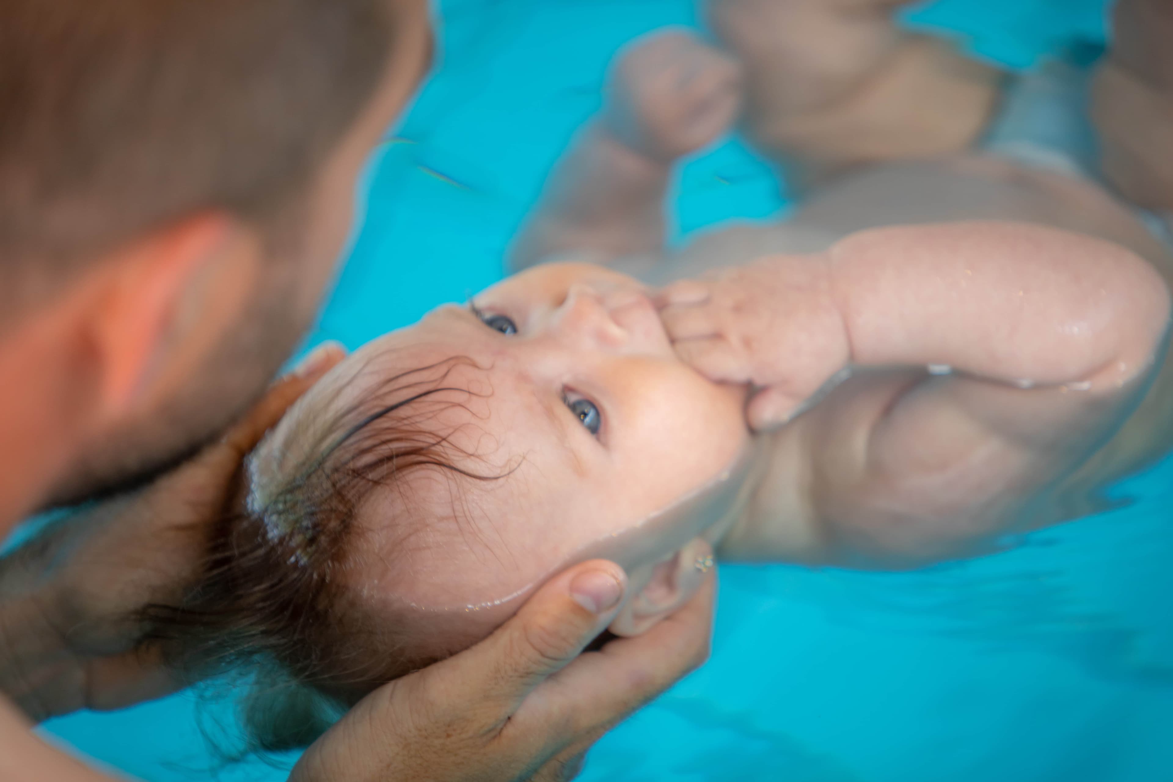 Háton lebegő baba, fejét a szülő tenyere támasztja alulról a vízben
